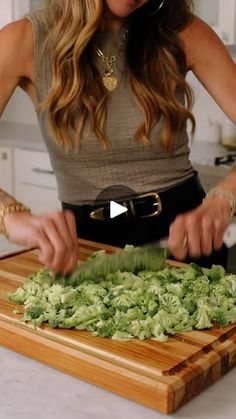 a woman cutting up lettuce on top of a wooden cutting board