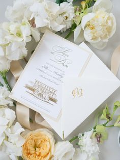 the wedding stationery is laid out on top of white flowers and ribbon, which are tied together