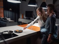 a man and woman standing in front of a kitchen counter with food on the stove