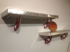 two metal shelfs are hanging on the wall next to each other, with red gears attached to them