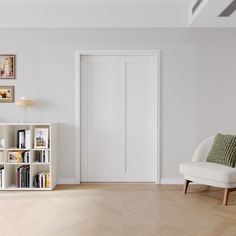 a living room with white walls and wooden floors, bookshelves and a chair