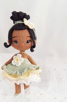 a crocheted doll is holding a flower in her hand and wearing a green dress