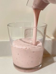 a person pouring milk into a glass filled with pink colored liquid on top of a white counter