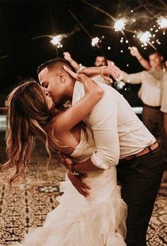 a bride and groom kissing on the dance floor with their sparklers in the air