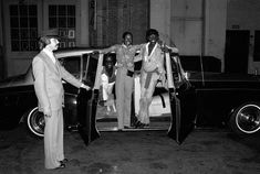 three men in suits are getting out of a car and shaking hands with one another