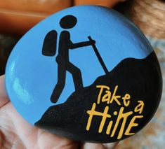 a hand holding a painted rock with the words take a hike on it