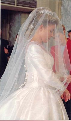 a woman in a wedding dress and veil walking down the aisle with people behind her