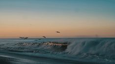 birds flying over the ocean at sunset with waves in the foreground and blue sky