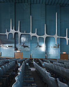 an empty auditorium with rows of blue chairs and ceiling fan in the center, looking towards the stage