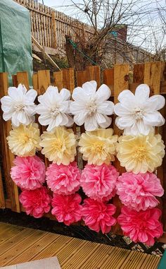 large paper flowers are arranged on a wooden fence