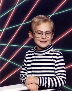 a young boy wearing glasses standing in front of a wall