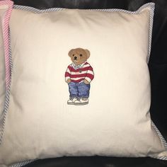 a white pillow with a teddy bear wearing a red and white striped shirt on it