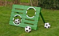 two soccer balls sitting in the grass next to a wooden structure that looks like a house