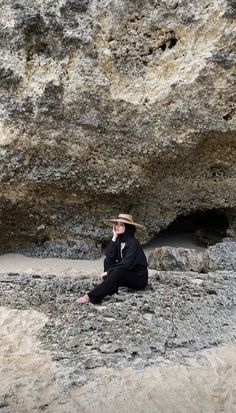 a man sitting on the ground next to a large rock