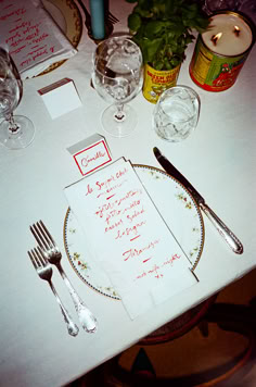 a place setting with silverware and menus on a white table cloth covered table