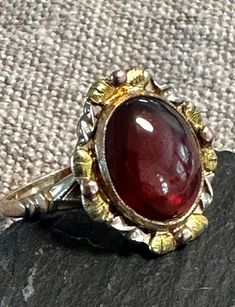 An early 1900s multi gold genuine red garnet cabochon ring.  Condition I see no problems the photos show the details.  Size 6 1/4, wt.- 3.3 grams, 2/3" north to south on finger.  A yellow gold ring with rose and green gold hand engraved Fram for the Garnet.  The detailing is crisp and artistic.  circa 1920-30, stamped 10K with Makers mark-DBA-American. Antique Ring, Gold Hand, Cabochon Ring, Gold Hands, Yellow Gold Ring, Early 1900s, Red Garnet, Hand Engraving, Antique Rings