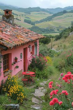 a small pink house sitting in the middle of a lush green field next to flowers