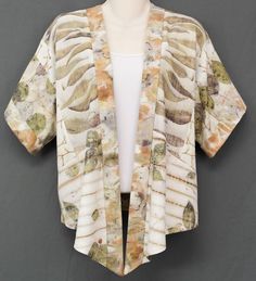 a mannequin wearing a white shirt and jacket with leaves on the front, standing in front of a gray background