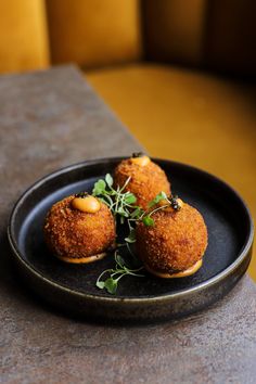 three fried food items on a black plate with green garnish and sprigs