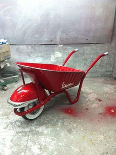 a red wheelbarrow sitting on top of a cement floor