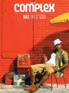 a man sitting on top of a chair under an umbrella next to a red wall