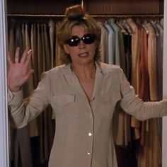 a woman wearing sunglasses standing in front of a closet full of shirts and ties with her hands out