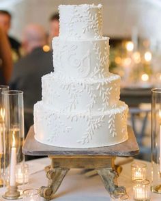 a large white wedding cake sitting on top of a wooden table next to some candles