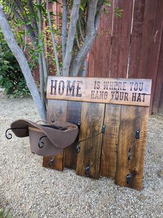 a wooden sign that says home is where you hang your hat next to a tree