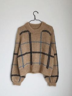 a sweater hanging on a hanger in front of a white wall with a black and tan checkered pattern