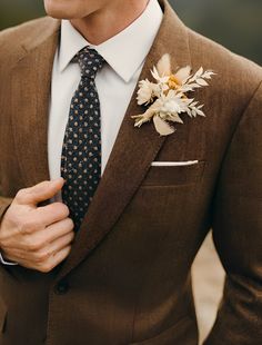 a man wearing a suit and tie with a flower on his lapel pin in his left hand