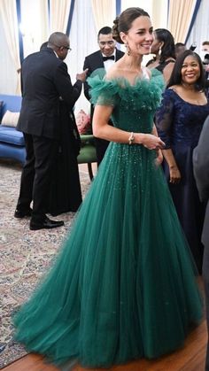 a woman in a green dress standing next to other people at a formal event and smiling