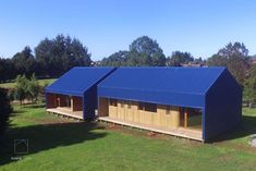 two large blue buildings sitting on top of a lush green field in front of trees