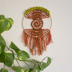 a plant is next to a wall hanging with a decorative item on it's side