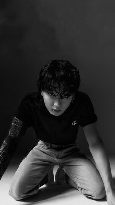 a man with tattoos sitting on the ground in front of a black and white photo