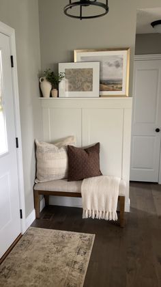 a bench with pillows on it in front of a door and some framed pictures above