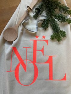 a white t - shirt with the word noel on it and a wooden spoon next to it