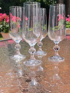 four wine glasses sitting on top of a table next to pink and red flowers in the background