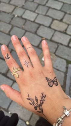 a person's hand with tattoos on it and two butterflies on the ring finger