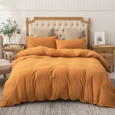 an orange comforter on a bed in a room with white walls and wooden flooring