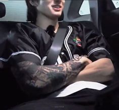 a man with tattoos on his arm sitting in a car