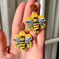 a hand holding two yellow and black bee earrings