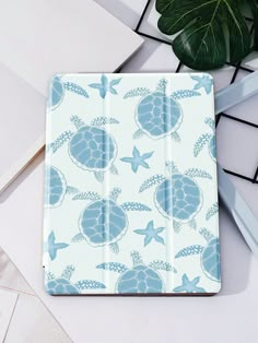 an ipad case with blue turtles and starfishs on it, next to a plant