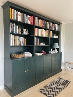 a bookshelf filled with lots of books next to a lamp and rug on top of a hard wood floor