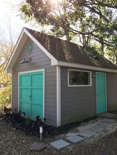 a small gray shed with a green door and window on the side of it, surrounded by trees