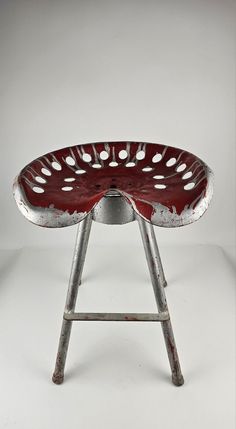 an old metal stool with holes in the middle and red paint on it's seat