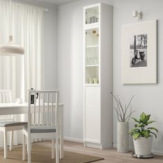 a white dining room table and chairs in front of a bookcase with pictures on the wall