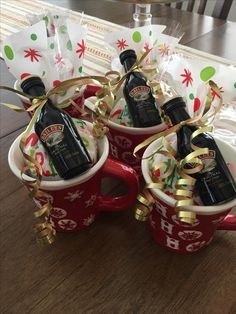 three coffee mugs filled with liquor bottles and wrapped in gold ribbon, sitting on a table