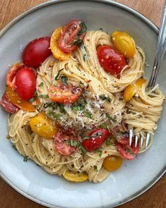 a white bowl filled with pasta, tomatoes and parmesan cheese on top of a wooden table