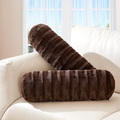 two pillows are sitting on the back of a white couch in front of a window