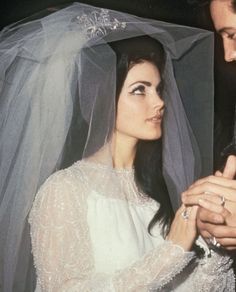 a man and woman standing next to each other in front of a white veil on their wedding day